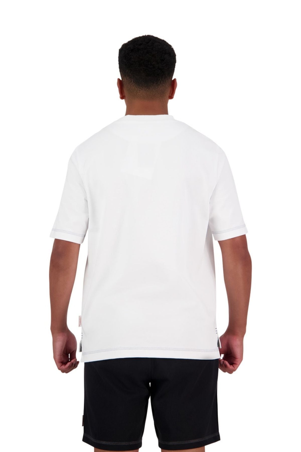 A person with short dark hair is shown from the back, wearing an oversized Canterbury CCC Collection T-Shirt and black shorts, standing against a white background.