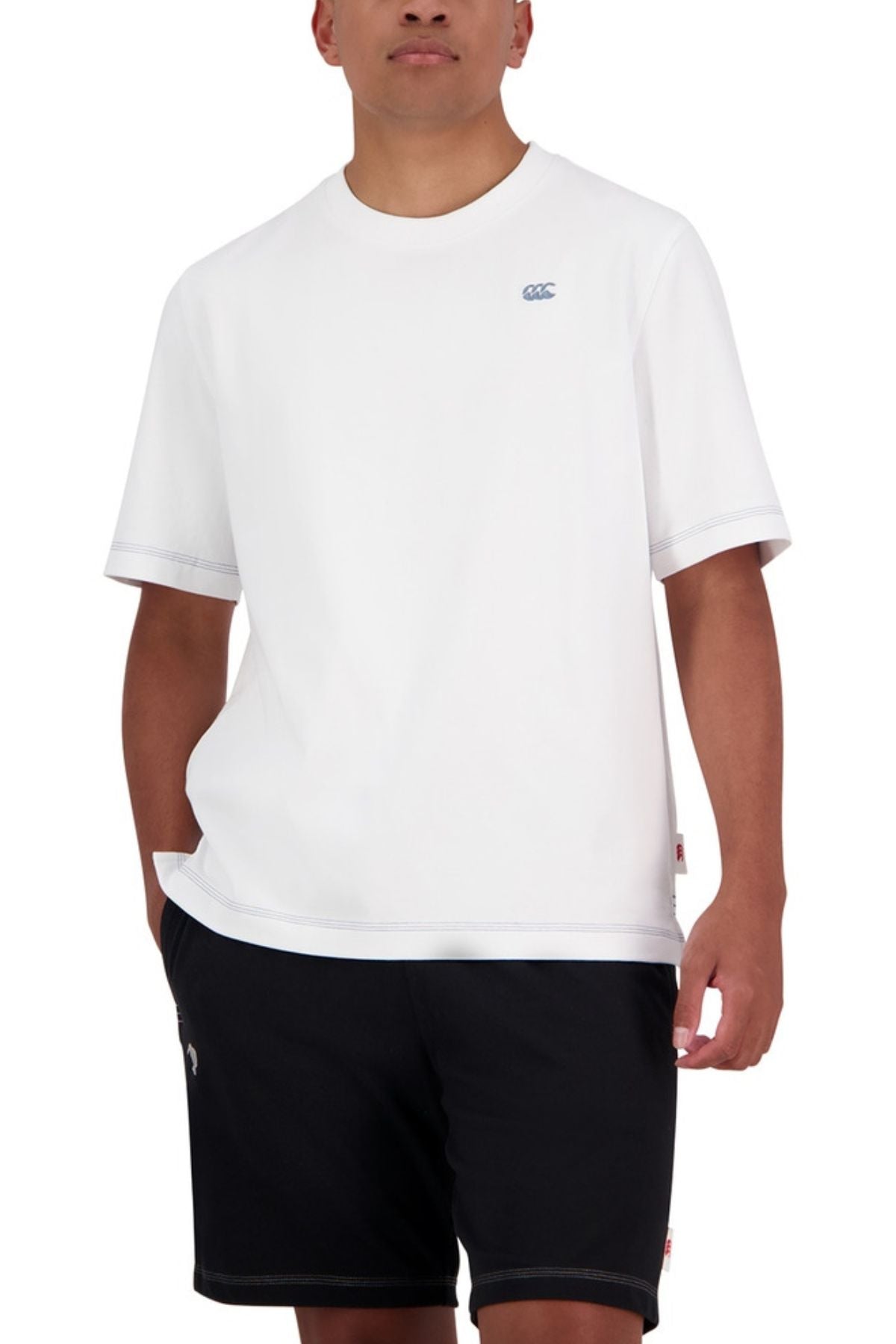 A person stands with one hand in their pocket, wearing an oversized fit Canterbury CCC Collection T-Shirt made from 100% cotton and black shorts, against a white background.