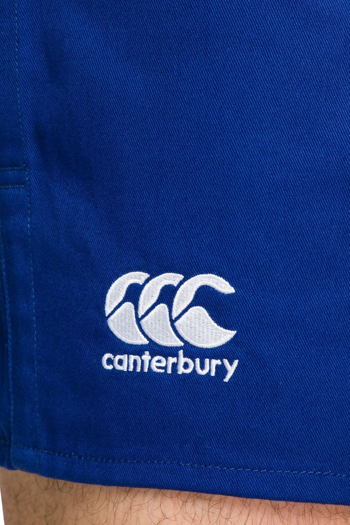 Here's a rewritten version of the sentence using the given product data:

A close-up of the Canterbury Rugged Drill Short in blue fabric highlights its elasticated waist and tape side pockets. The distinctive Canterbury logo, featuring three overlapping white curves with "canterbury" embroidered below, enhances its unique style.