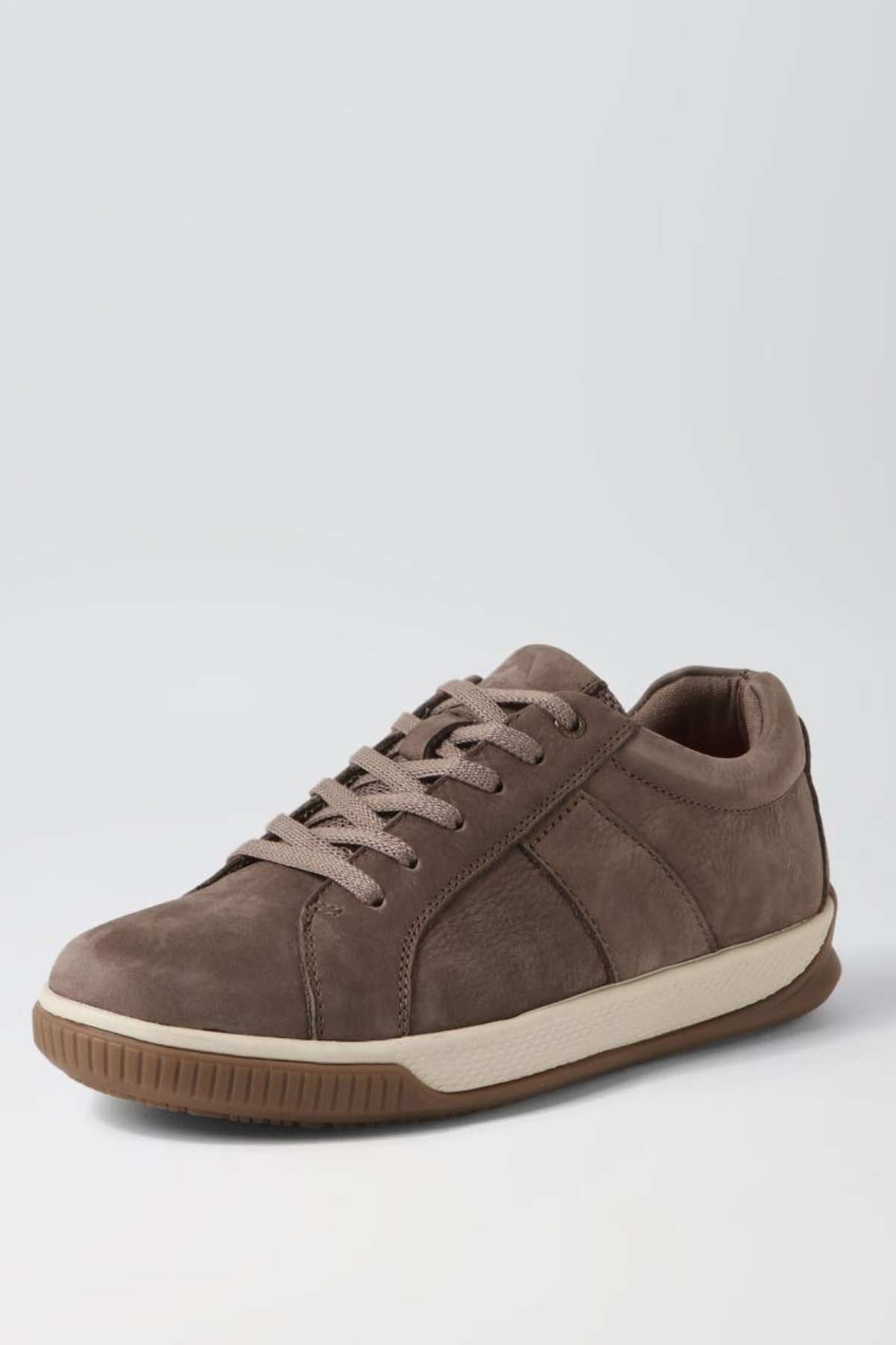 The Colorado Edo Sneaker is a casual, low-top shoe made of brown suede with beige laces and a beige rubber sole. It features intricate stitching along the sides and toe area, with the sole extending slightly over the toe for added protection. The image background is light gray.