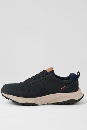 The Colorado Suzuki Shoe is a black athletic sneaker made from premium leather, with black laces, a thick beige slip-resistant sole, orange detailing by the heel, and a tan tongue accent, shown on a plain light gray background.