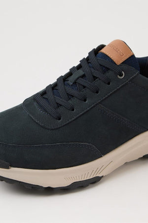 A close-up of the Colorado Suzuki Shoe reveals dark blue suede, navy laces, a beige slip-resistant sole, and a brown leather tongue accent with embossed text.