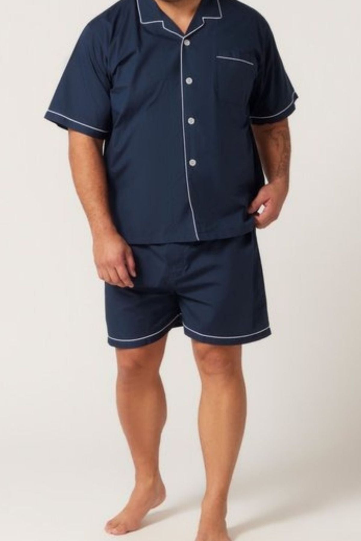 A person stands barefoot against a plain background, wearing the Contare Country Cotton Rich Short Sleeve Classic Set—a matching navy blue button-up shirt and men's boxer shorts with white piping.