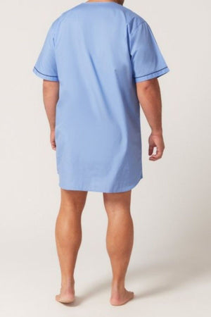A person stands barefoot, facing away from the camera, wearing the Contare Country Cotton Rich Short Sleeve Nightshirt in light blue. The background is plain and light-colored.