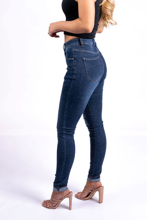 A woman poses in Country Denim Skinny Jeans, paired with a black crop top and tan high-heeled sandals, against a plain white background.