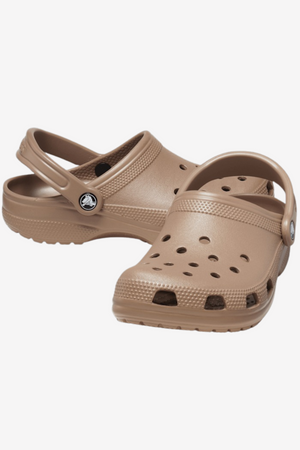 A pair of Crocs Classic Clogs in brown, featuring upper ventilation ports and adjustable heel straps. With textured front and sides, these shoes display the logo on the straps. Ideal for any water adventure, these clogs offer exceptional comfort and durability.