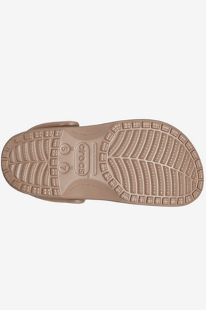 The image displays the underside of a Crocs Classic Clog in beige, showcasing anti-slip patterns, circular grips, and the engraved "Crocs" brand name at the center along with size markings—ideal for your next water adventure.