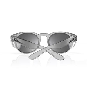 A pair of stylish, grey SafeStyle Cruisers Graphite Frame Tinted Lens sunglasses with dark lenses is shown, with the arms crossed in an X shape. The brand logo is engraved on the sides of the arms, and the glasses, boasting UV400 protection and safety ratings, are positioned against a plain white background.