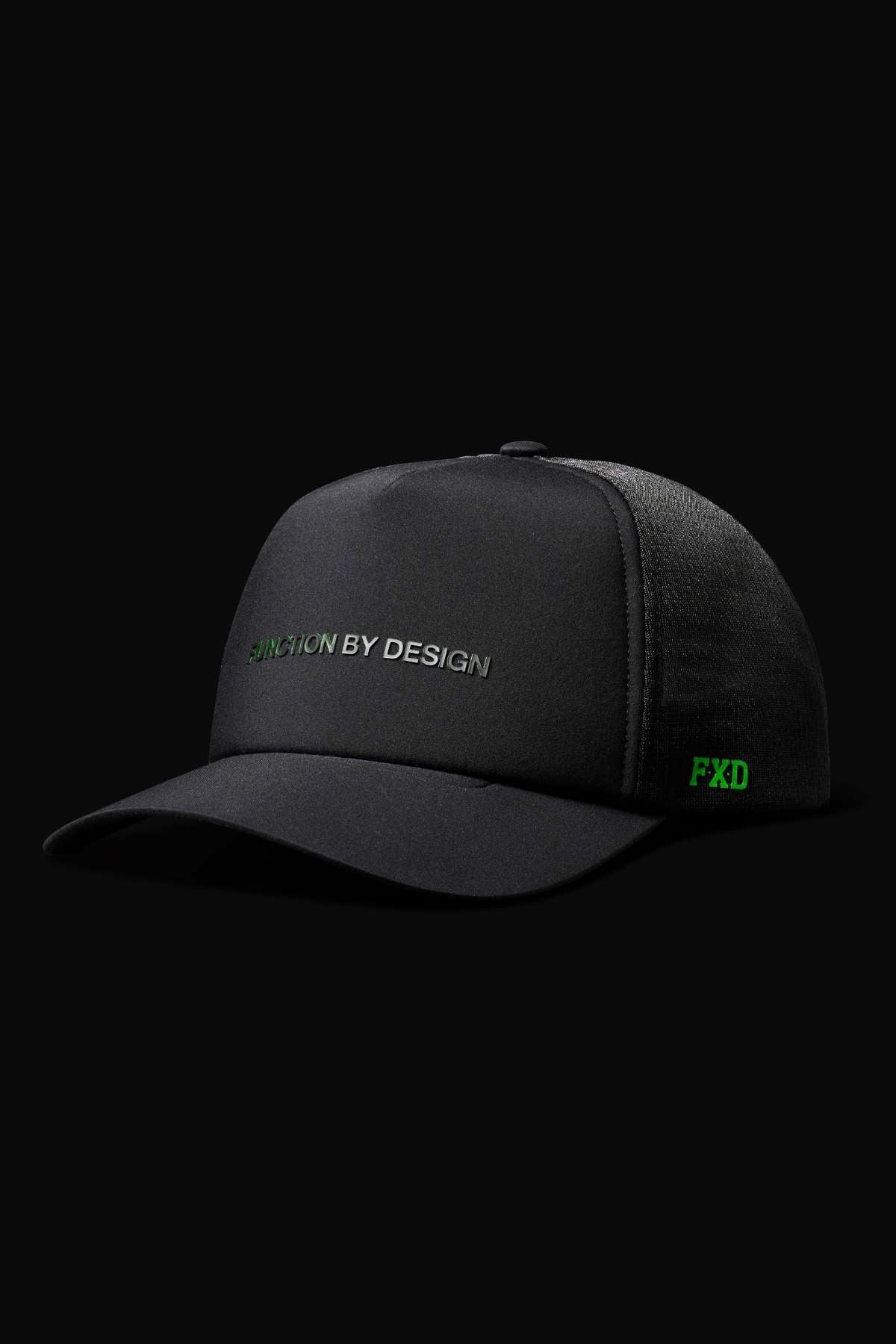 The FXD CP-13 Trucker Cap is black with "FUNCTION BY DESIGN" embroidered in green and white on the front, "FXD" in green on the side, and made from breathable fabric. Photographed against a black background.