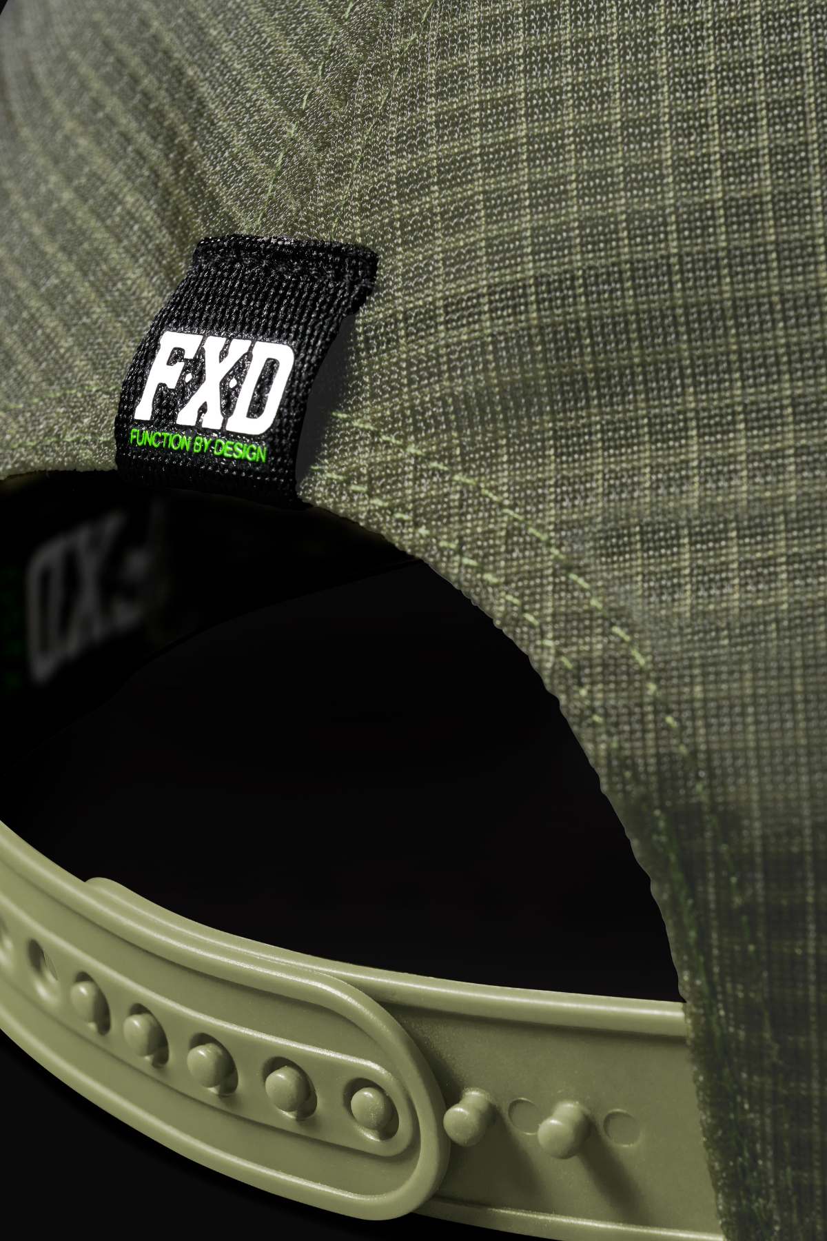 Close-up of the back of the FXD CP-13 Trucker Cap in olive green, showing its grid texture, breathable material, adjustable snapback strap, and a black label with "FXD FUNCTION BY DESIGN" in white and green text.