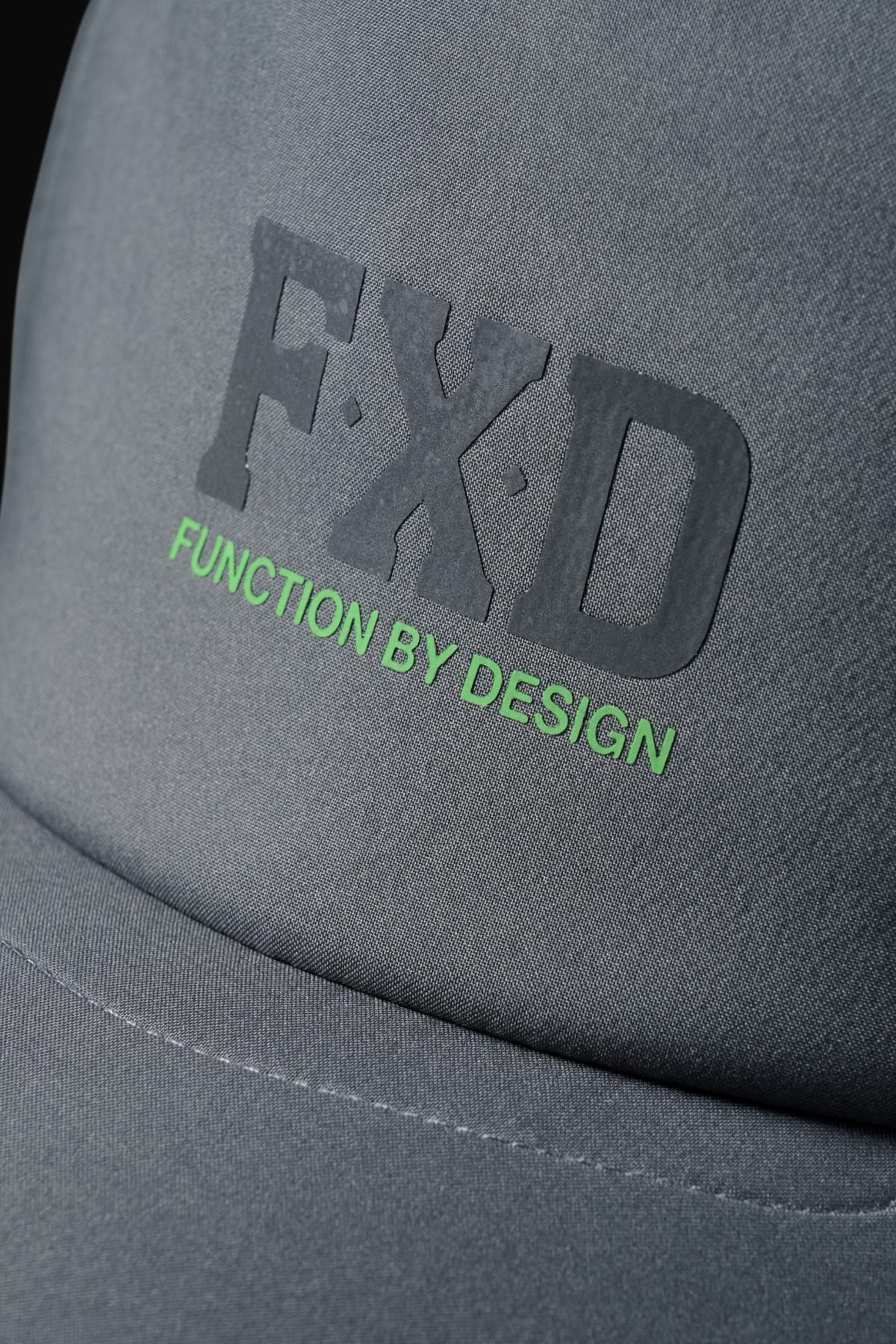 Close-up of the FXD CP-13 Trucker Cap in gray, made from breathable fabric, with raised black "FXD" lettering and green "FUNCTION BY DESIGN" text below.