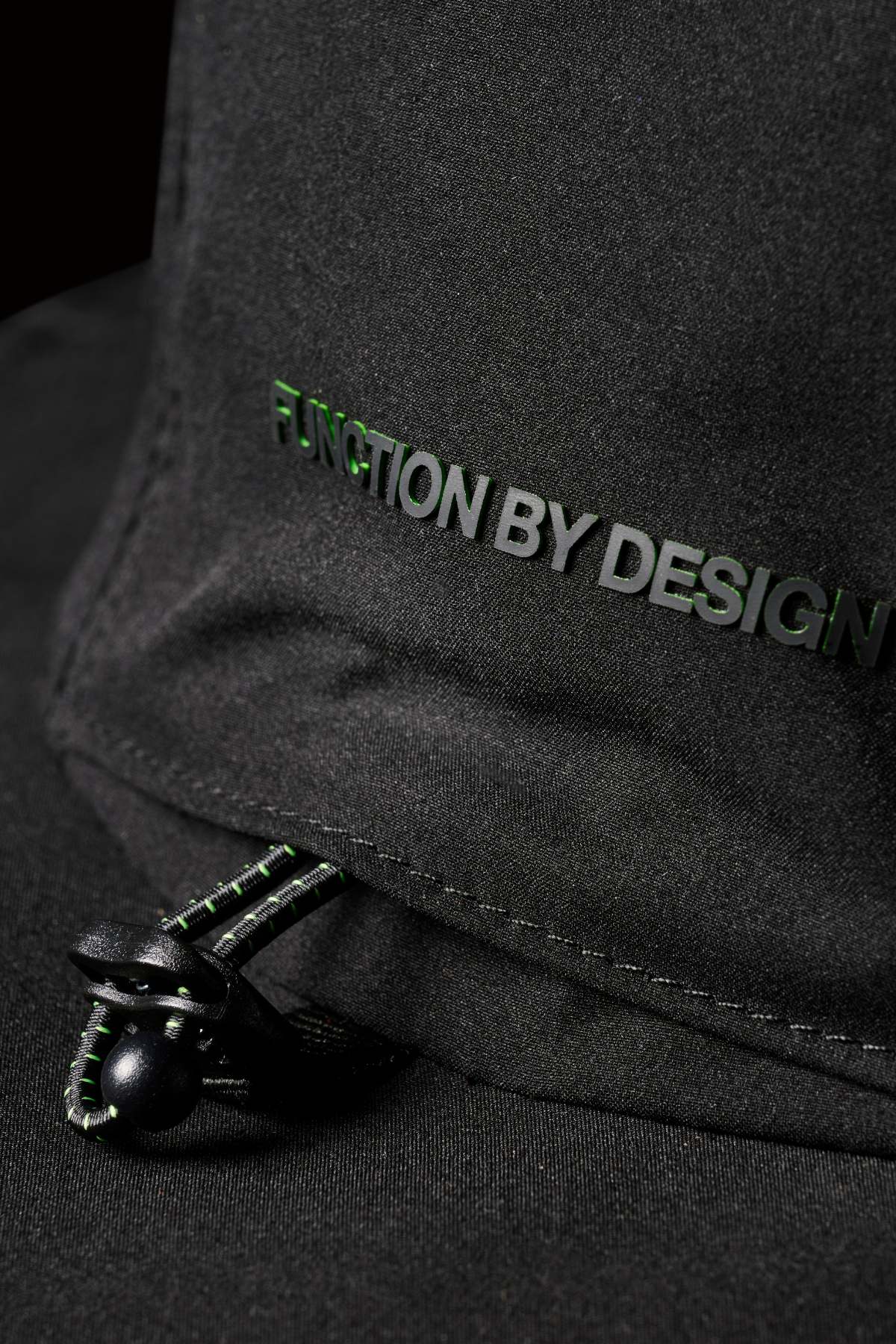 Close-up of the FXD CP-14 Boonie Hat in black, featuring "FUNCTION BY DESIGN" embroidered in green and black. This lightweight hat includes a black drawstring, green stitching, and a plastic toggle for sun protection.