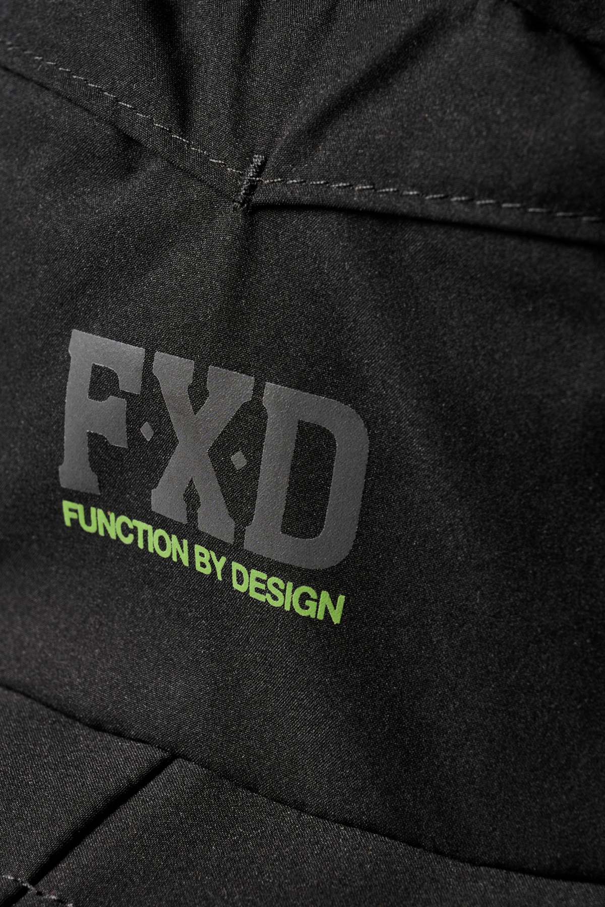 Close-up of the FXD CP-14 Boonie Hat’s black fabric: bold grey "FXD" and green "FUNCTION BY DESIGN" text, visible stitching, and lightweight construction for enhanced sun protection.