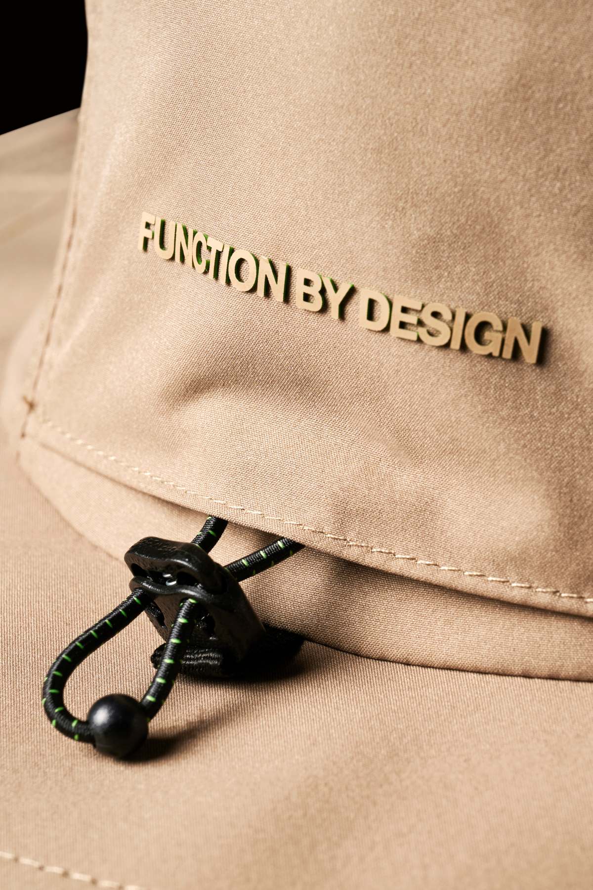 Close-up of the FXD CP-14 Boonie Hat featuring a beige fabric with "FUNCTION BY DESIGN" embroidered on it. Below, a black adjustable drawstring with a toggle ensures sun protection and an optimal fit.
