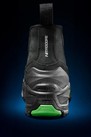 The FXD DURA X-3 Slip On Work Boots are shown from the back in black and gray, with a pull tab, "NITROCORE" branding, green sole accent, and a rugged NITROCORE sole system—set against a dark gradient background.