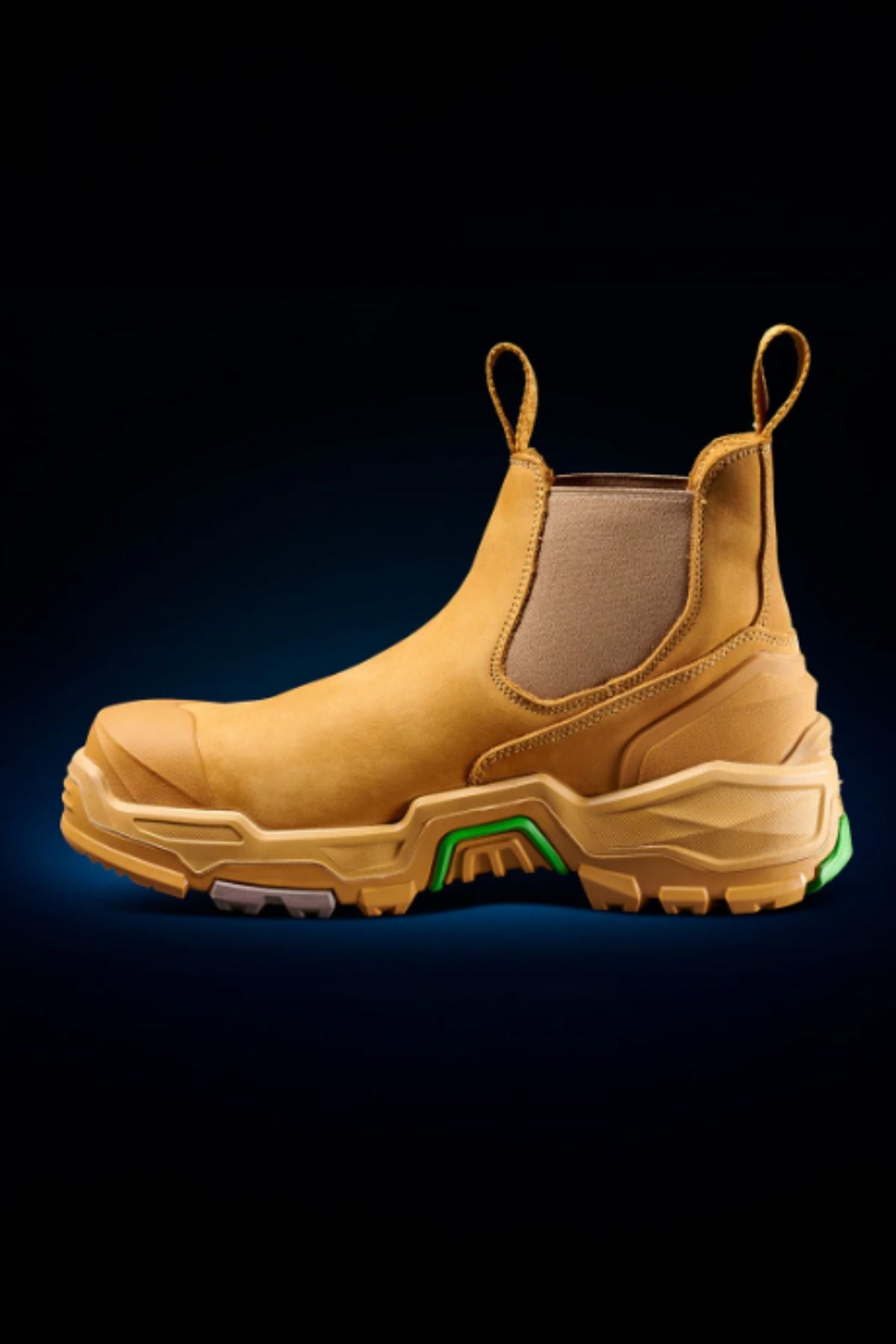 The FXD DURA X-3 Slip On Work Boots are tan, rugged industrial boots with chunky, puncture-resistant soles and front and back pull tabs, featuring green and gray accents on the sole.