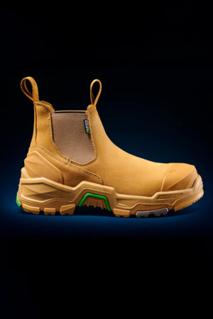 The FXD DURA X-3 Slip On Work Boots, shown on a black background, feature a tan color, rugged tread, elastic side panels, and a green accent near the sole.