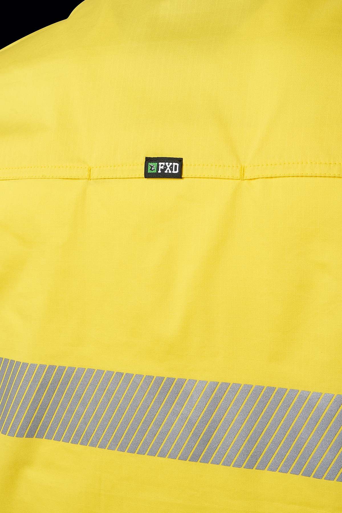 A close-up of a high-visibility yellow jacket with reflective tape across the back. Above the stripe, there is a small black and green logo with the text "FXD". The material appears smooth and durable, resembling an FXD LSH-2T Stretch Taped Hi Vis Long Sleeve Work Shirt.