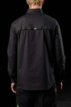 A blond-haired person is seen from behind in a solid black setting, wearing the FXD LSH-3 Vented Work Shirt and black pants with green and white logo tags. The outfit features lightweight stretch fabric for all-day comfort.