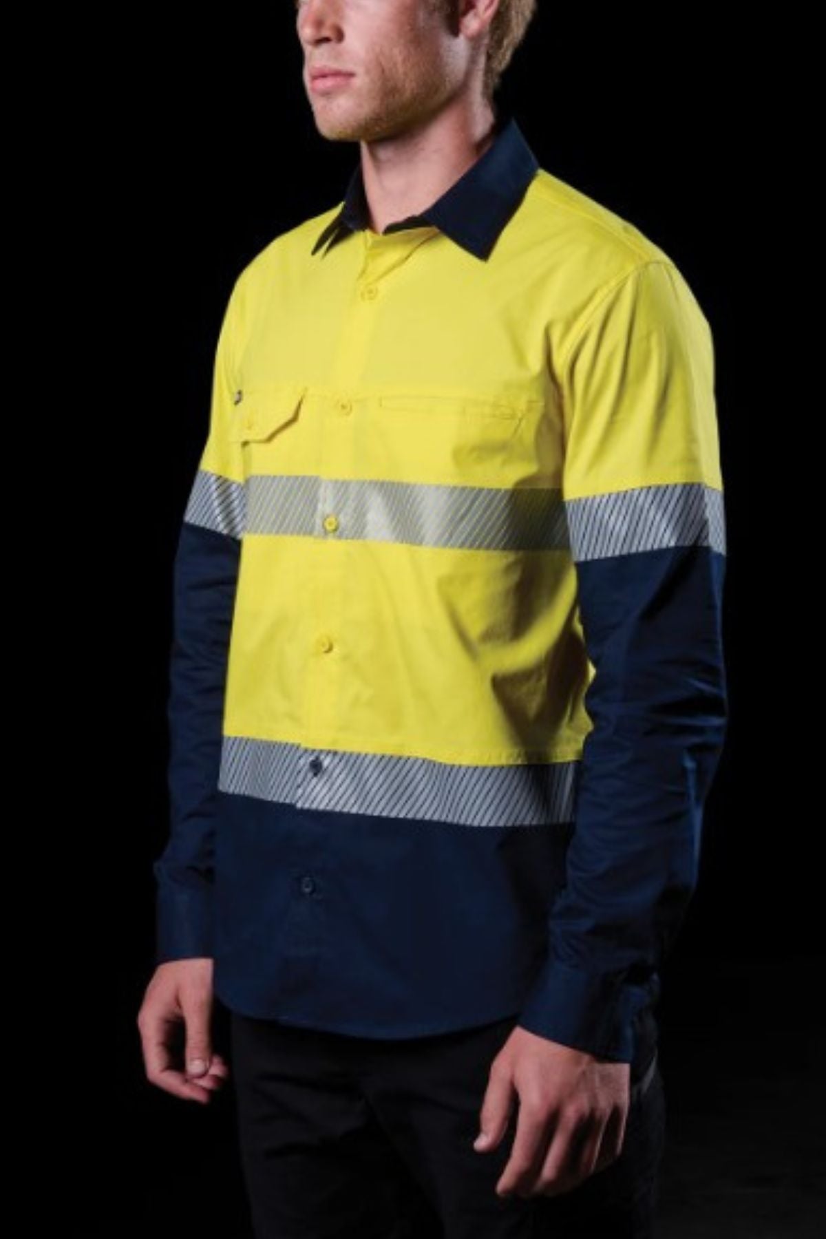 Wearing the FXD LSH-4T Work Shirt with yellow and navy panels, segmented reflective tape, and made from lightweight durable stretch fabric, a person stands against a black background.