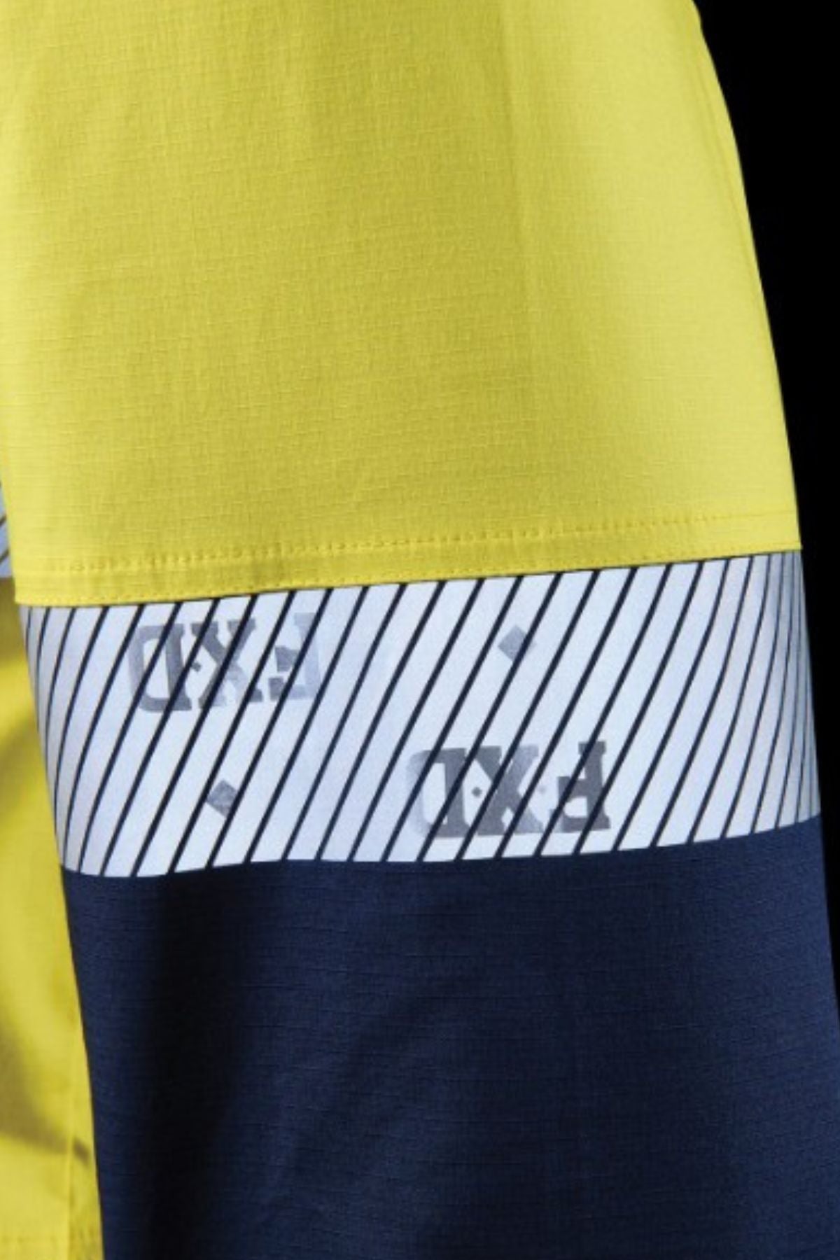 A close-up of the FXD LSH-4T Work Shirt, showing three sections: bright yellow on top, a white stripe with diagonal black lines and faded text in the center, and dark blue fabric at the bottom.