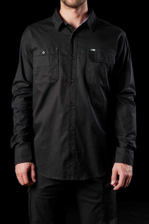 A person wearing the FXD LSH-1 Stretch Work Shirt, a long-sleeved black button-up with two chest pockets, stands against a black background. The durable shirt has a professional appearance, and the person's hands are at their sides.