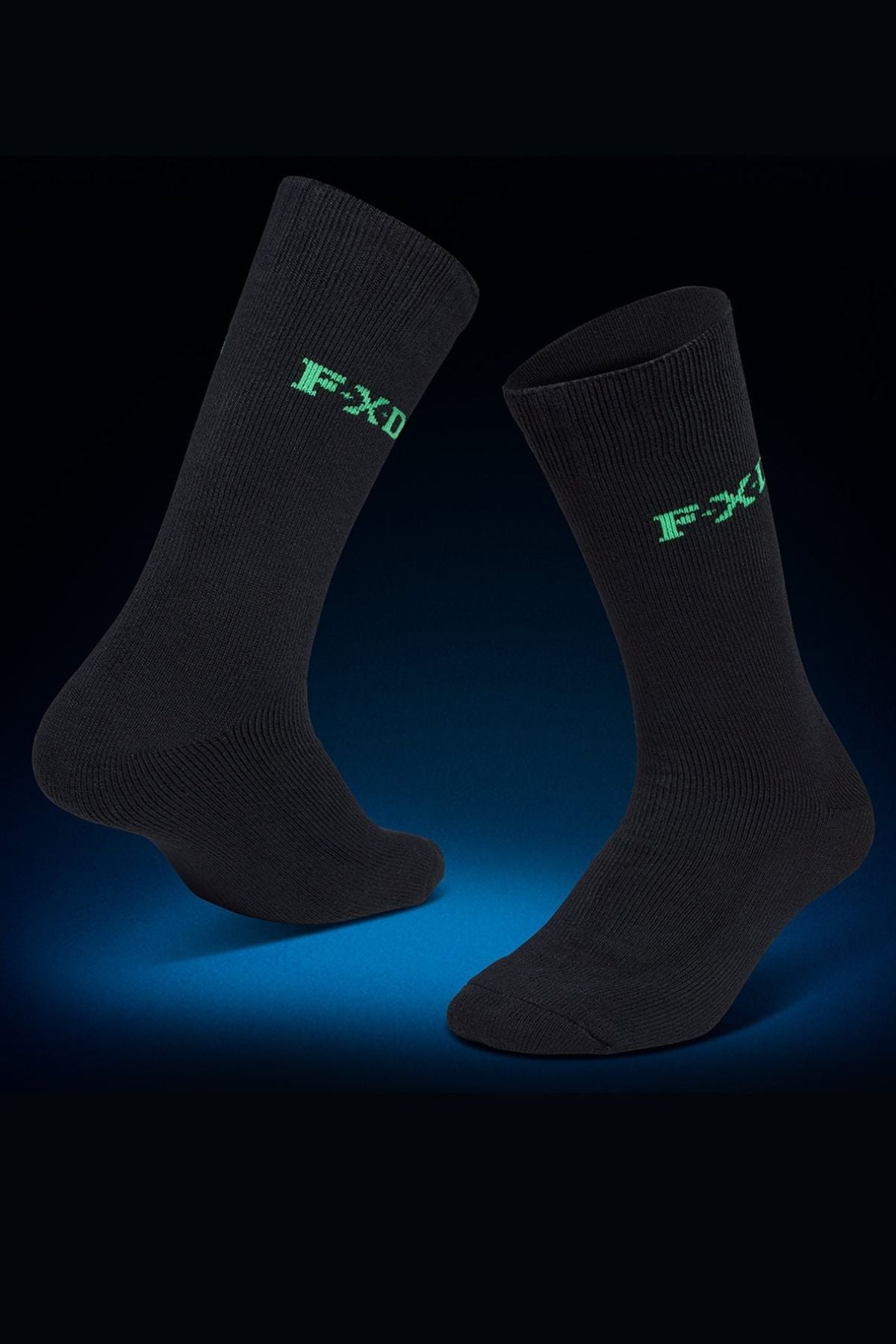 Two black FXD SK-5 Bamboo Socks with green "FXD" text near the top are shown on a dark blue gradient background. One sock stands upright, while the other floats at an angle, emphasizing style and comfort. Pack contains 2 socks.
