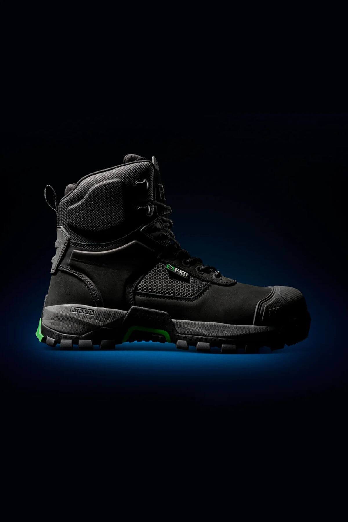 The FXD WB-1 Work Boot, a black heavy-duty work boot with green accents and a thick, rugged, slip-resistant sole, is displayed against a dark background. The boot features a high ankle design with reinforced toe and heel areas, including a safety toe, and visible branding on its side.