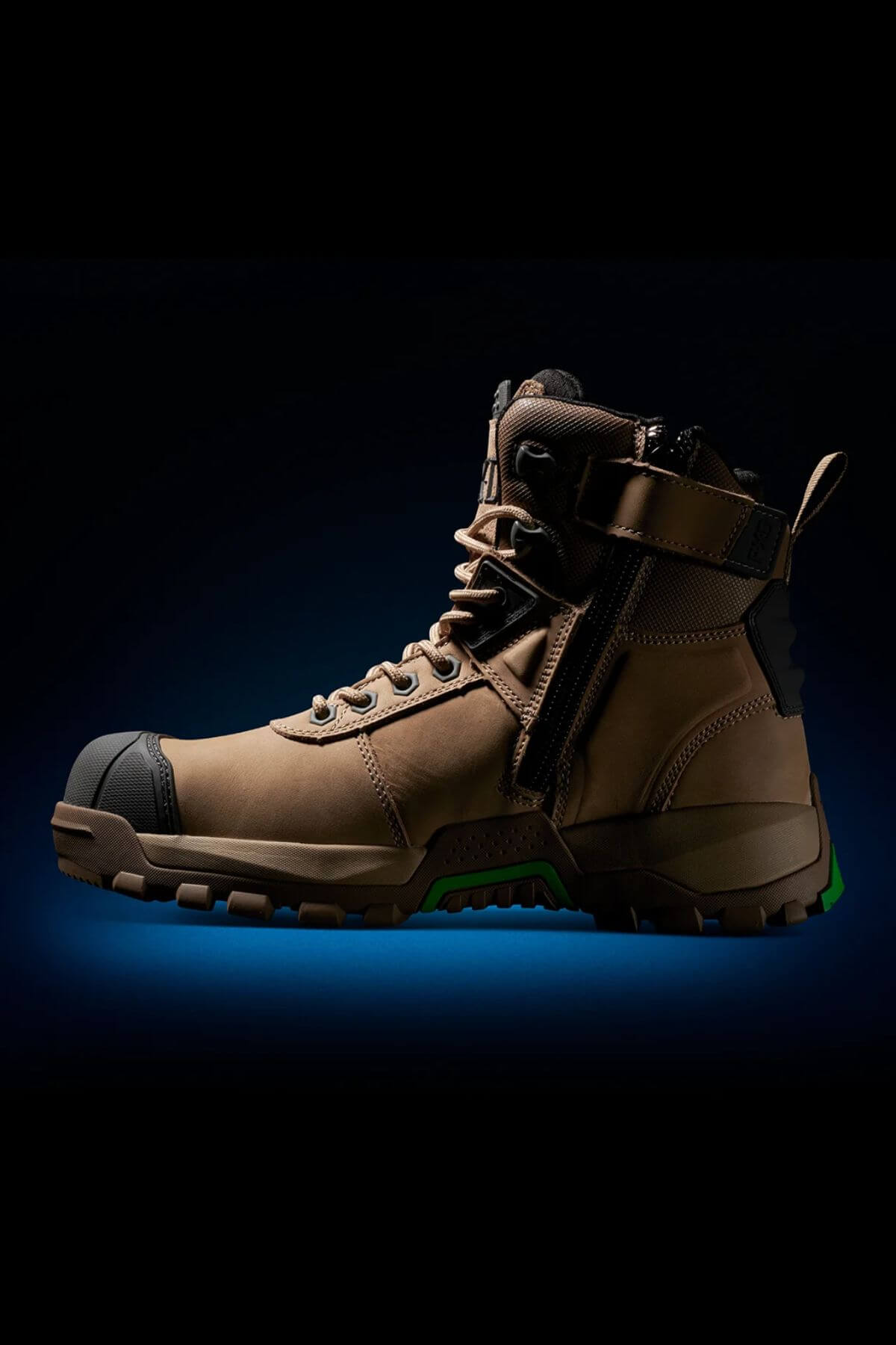 The FXD WB-1 Work Boot is a rugged, tan-colored work boot featuring green details and a side zipper, set against a dark gradient background. Equipped with a safety toe and a heavy-duty sole with deep treads, it’s perfect for rough terrain. The laced-up high ankle provides added support, while its slip-resistant design ensures secure footing.
