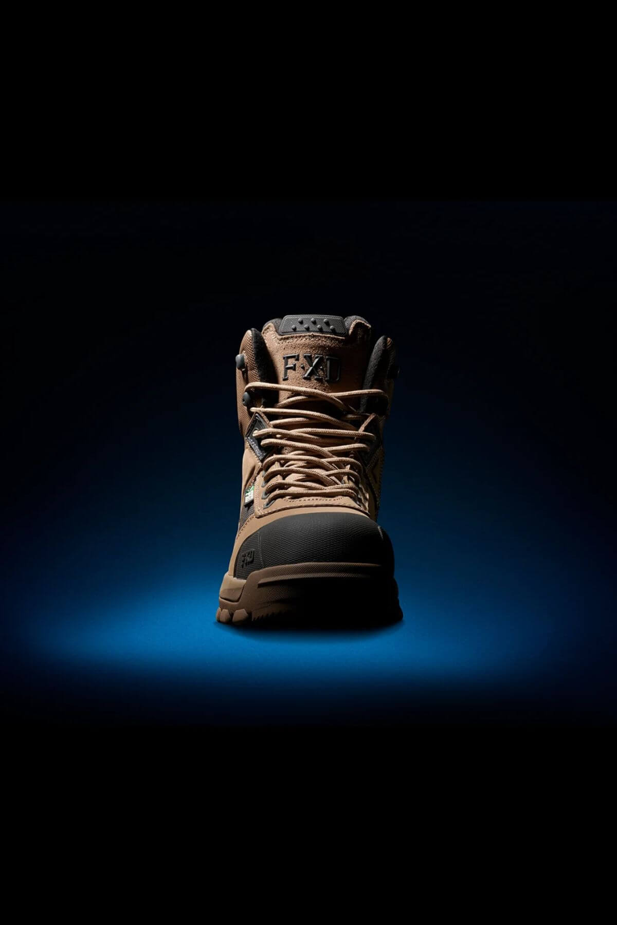 The FXD WB-1 Work Boot, featuring yellow laces, stands out against a dark blue background. The well-lit setting accentuates its rugged design, intricate details, and safety toe feature.