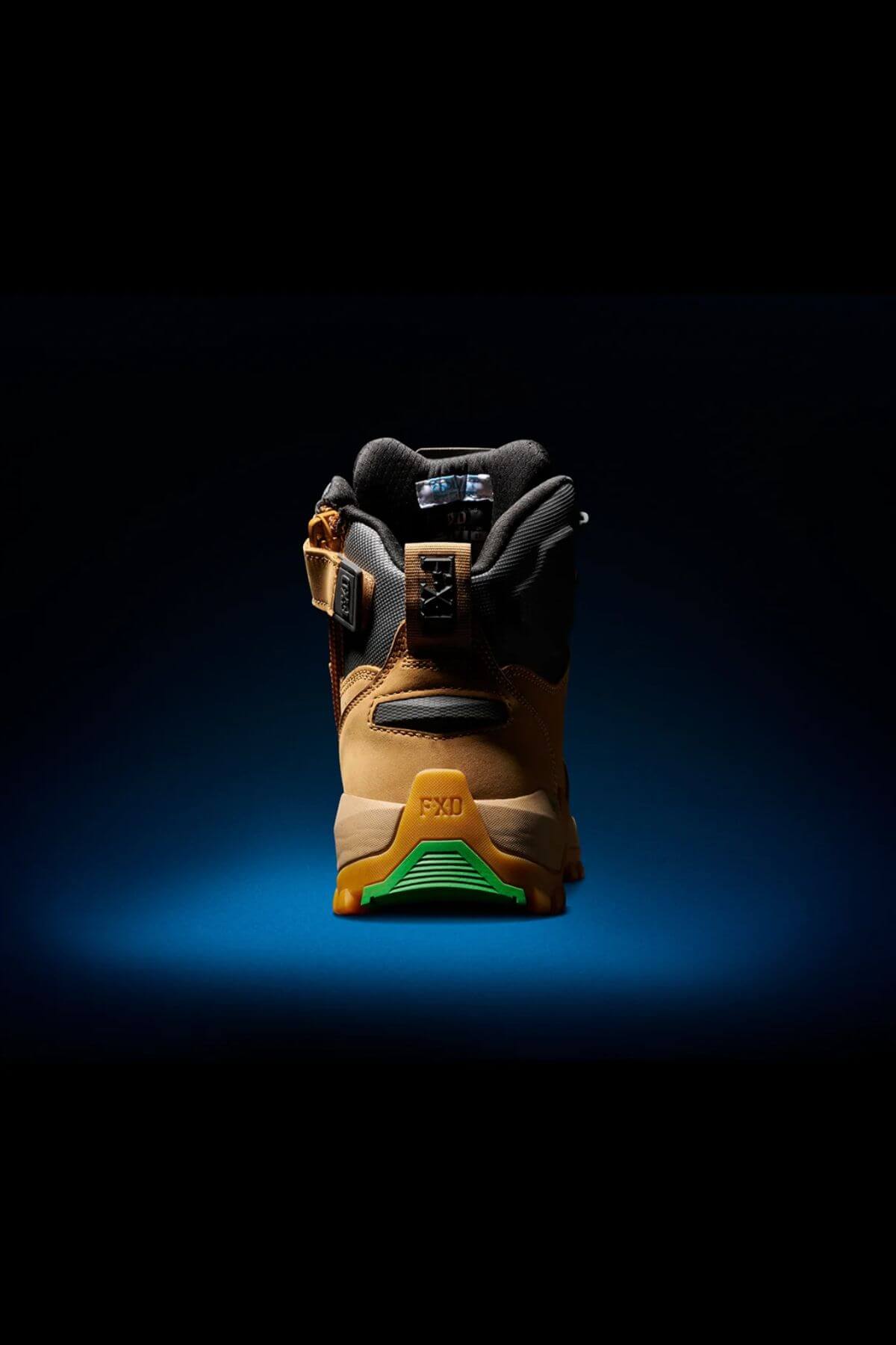 A brown and black FXD WB-2 Work Boot is displayed against a dark background. The shoe boasts a green slip-resistant sole, black laces, a safety toe, a logo patch on the tongue, and the letters "FXD" embossed on the back. The high-top boot is well-lit, emphasizing its details and texture.
