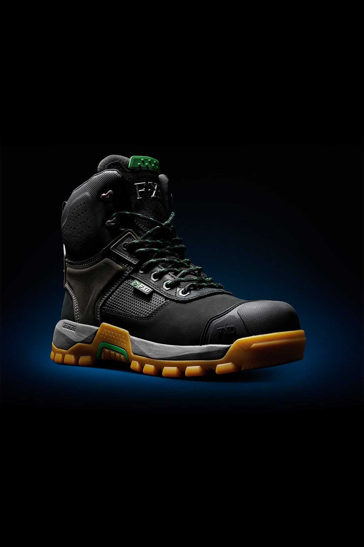 A close-up shot of the FXD WB-1 Work Boot with a rugged design showcases its black, high-top structure. It features a thick, yellow-brown sole and green lace accents, complemented by a cushioned collar. The sturdy construction of the boot is enhanced by its composite safety toe and NITROLITE midsole cushioning, all set against a dark background.