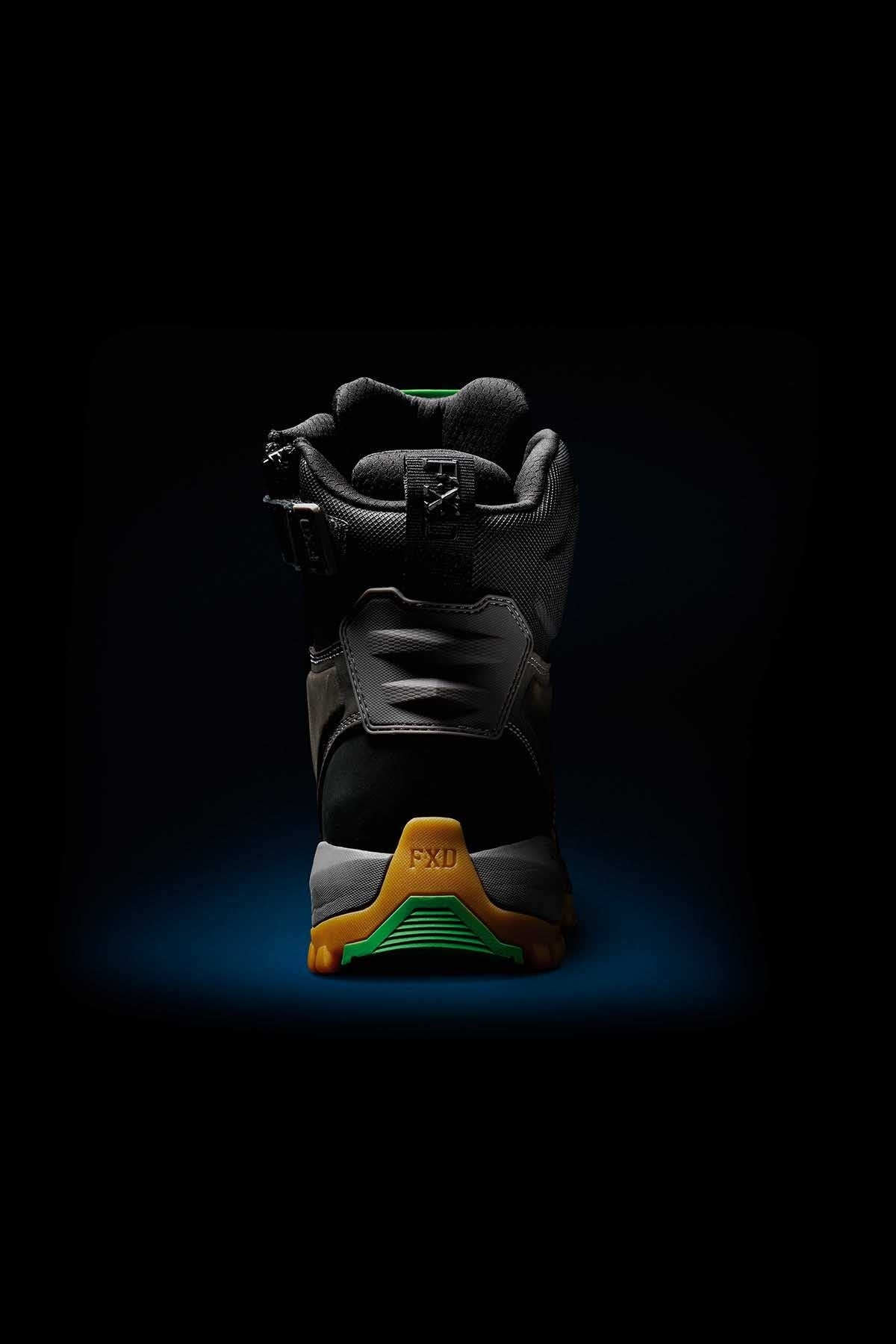 The image showcases the FXD WB-1 Work Boot against a dark background. This black boot sports green and yellow accents, with a prominent yellow heel cap at the back inscribed with "FXD." The sturdy design of the boot is highlighted, featuring a composite safety toe and NITROLITE midsole cushioning for enhanced comfort.
