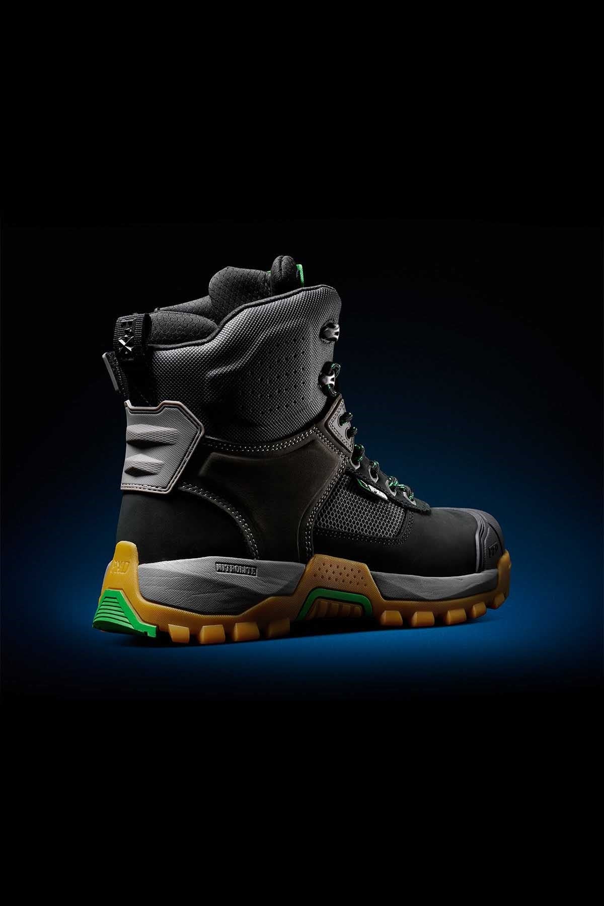 The FXD WB-1 Work Boot is a high-top, rugged black work boot with a thick, textured sole featuring brown and green accents. It includes a padded ankle area, metallic eyelets for laces, reinforced toe and heel sections, and composite safety toe protection.