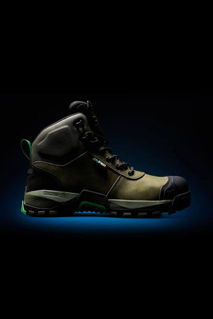 The FXD WB-2 Work Boot features a rugged olive green and black design, a reinforced toe, thick tread sole, NITROLITE midsole cushioning, and green accents. Shown against a dark background with a subtle blue glow underneath.