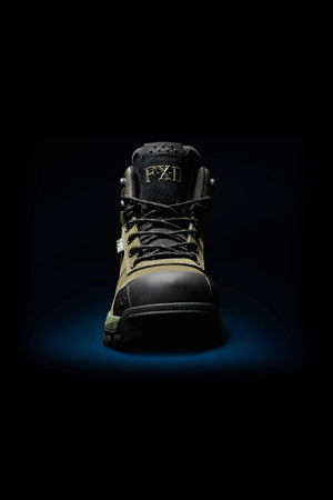 An FXD WB-2 Work Boot in black and olive green, with a composite safety toe and black laces, is centered under a spotlight on a dark background. The "FXD" logo appears on the tongue.