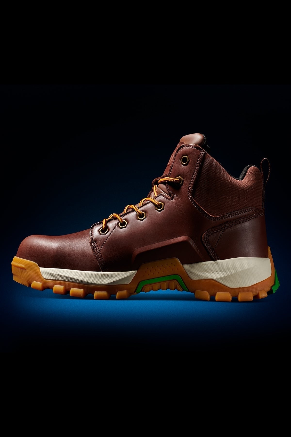 The FXD WB-3 Work Boot features premium leather, yellow laces, a tan midsole, and a rugged orange and green rubber outsole, pictured on a dark background.