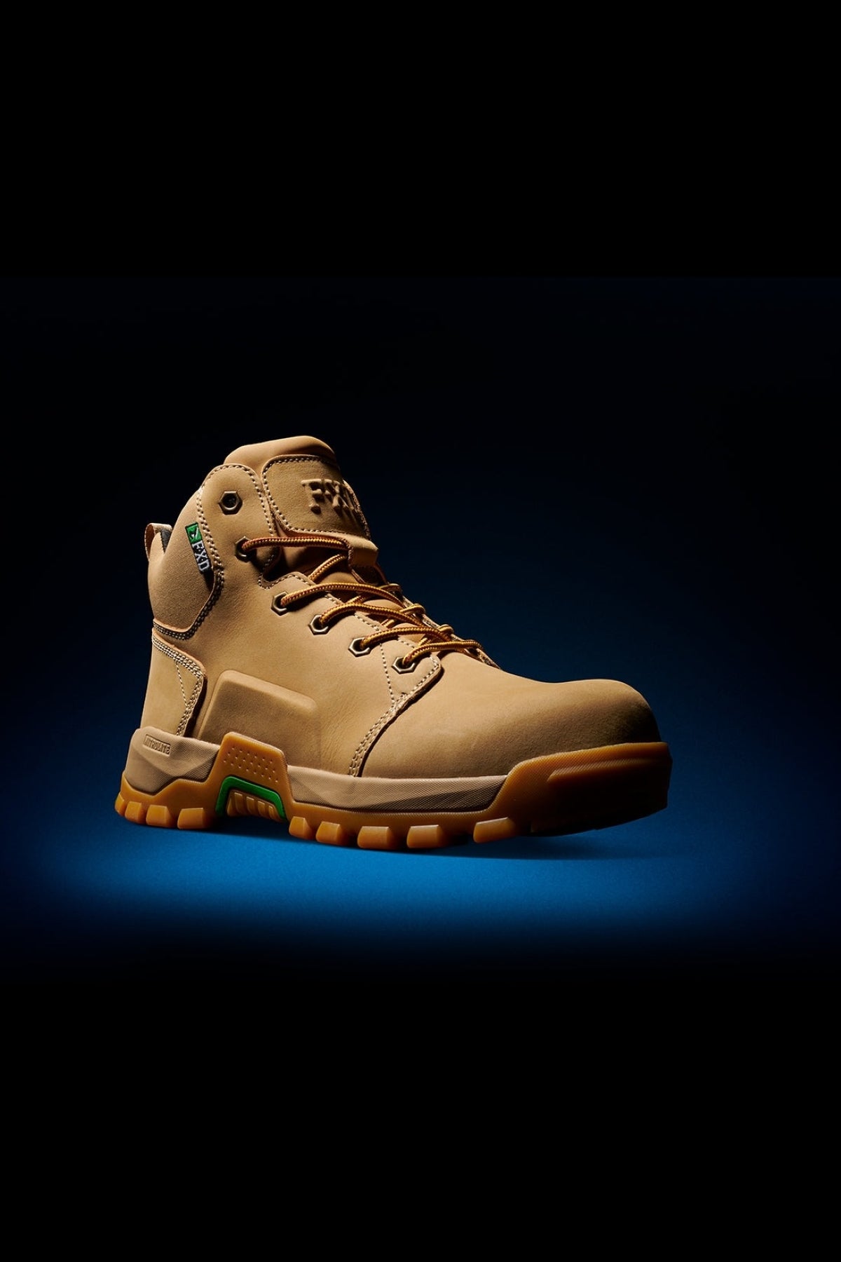 The FXD WB-3 Work Boot is a tan high-top design with brown laces, crafted from premium leather. It features a thick orange-treaded sole and a green side tag, set against a dark gradient background.