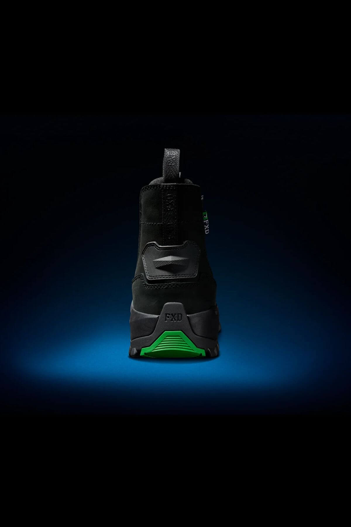 The FXD WB-4 Work Boot is displayed from the back against a dark background, with a gradient blue spotlight highlighting its form. Made from nubuck leather, the boot features a green sole prominently branded with "FXD." The durable work boot's safety toe design conveys ruggedness and reliability.