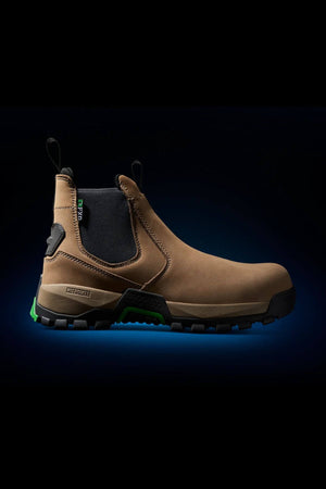 The FXD WB-4 Work Boot features a brown slip-on design with black elastic side panels and pull tabs, complemented by a rugged black sole. Green accents enhance the sole and heel, adding a touch of style. The slip-resistant boot is showcased against a black background with a subtle blue glow.

