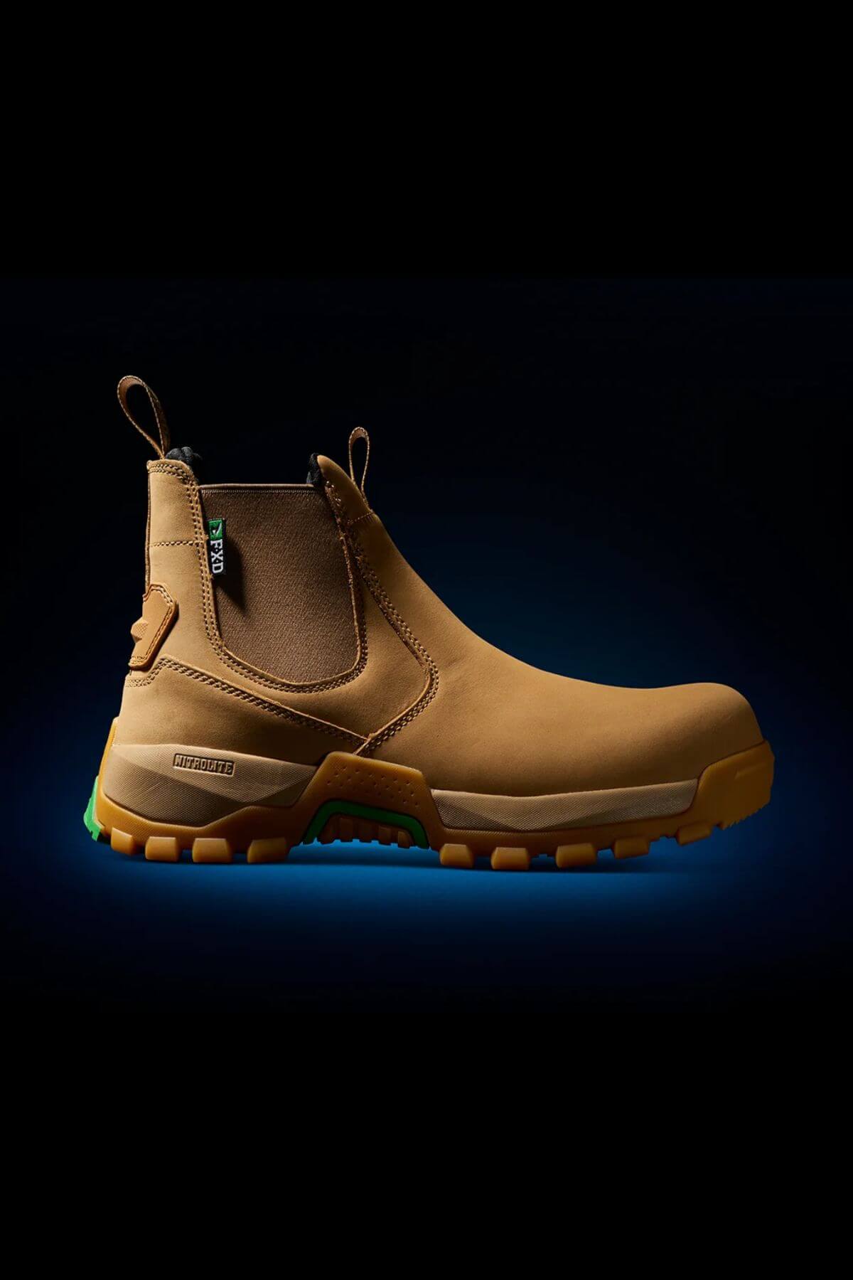 The FXD WB-4 Work Boot, a tan, rugged work boot with a pull-on design and safety toe, features durable rubber soles and green accents. Centered against a dark gradient background, the boot displays brand tags and appears designed for heavy-duty use or outdoor activities.
