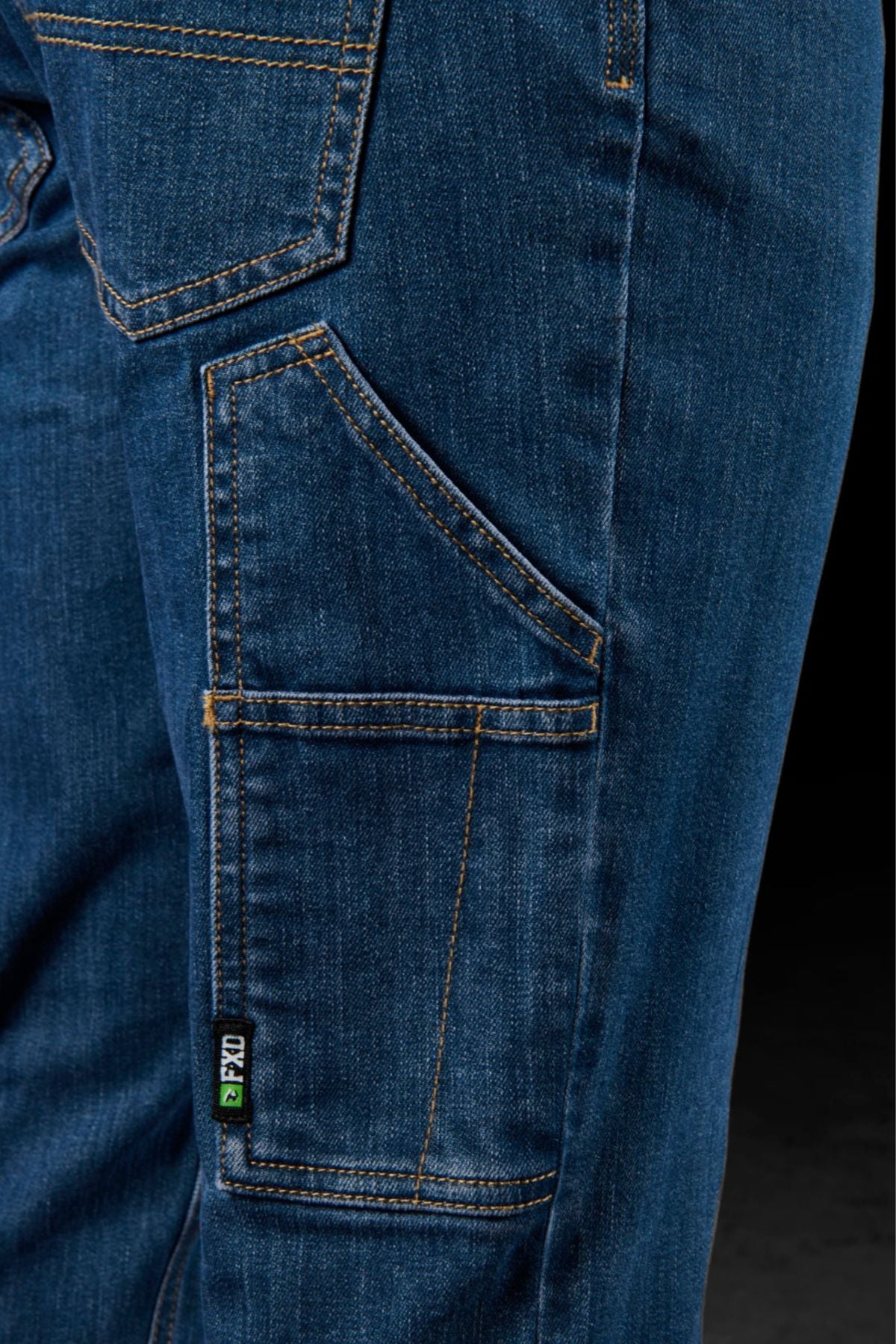 Close-up of the side pocket and stitching details on FXD WD-4 blue denim jeans, made from COOLMAX EcoMade fabric, featuring a small green and black "FXD" label by the pocket seam.