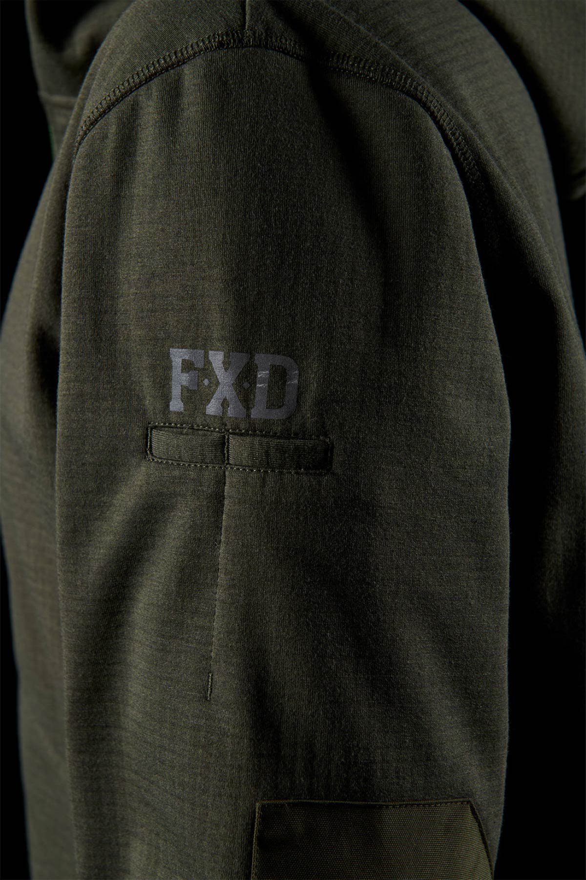 Close-up of a dark green sleeve from the FXD WF-3 Jacket, featuring "FXD" printed in gray above a small horizontal pocket on durable fabric—a reliable workwear choice for tough environments.