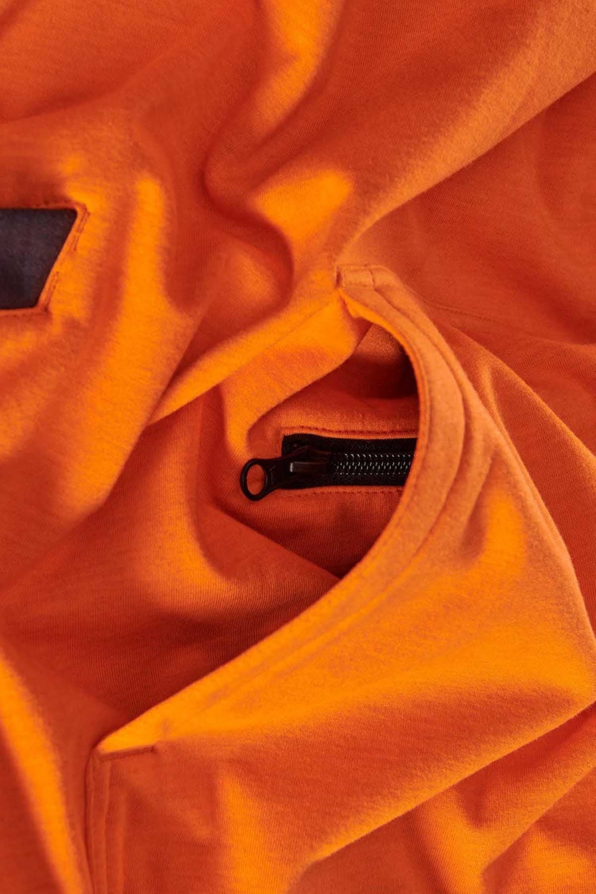 A close-up of the FXD WF-1 Hoodie's orange fabric features a partially open black zipper. The material, resembling water-resistant fleece, displays some folds and creases around the zippered pocket.
