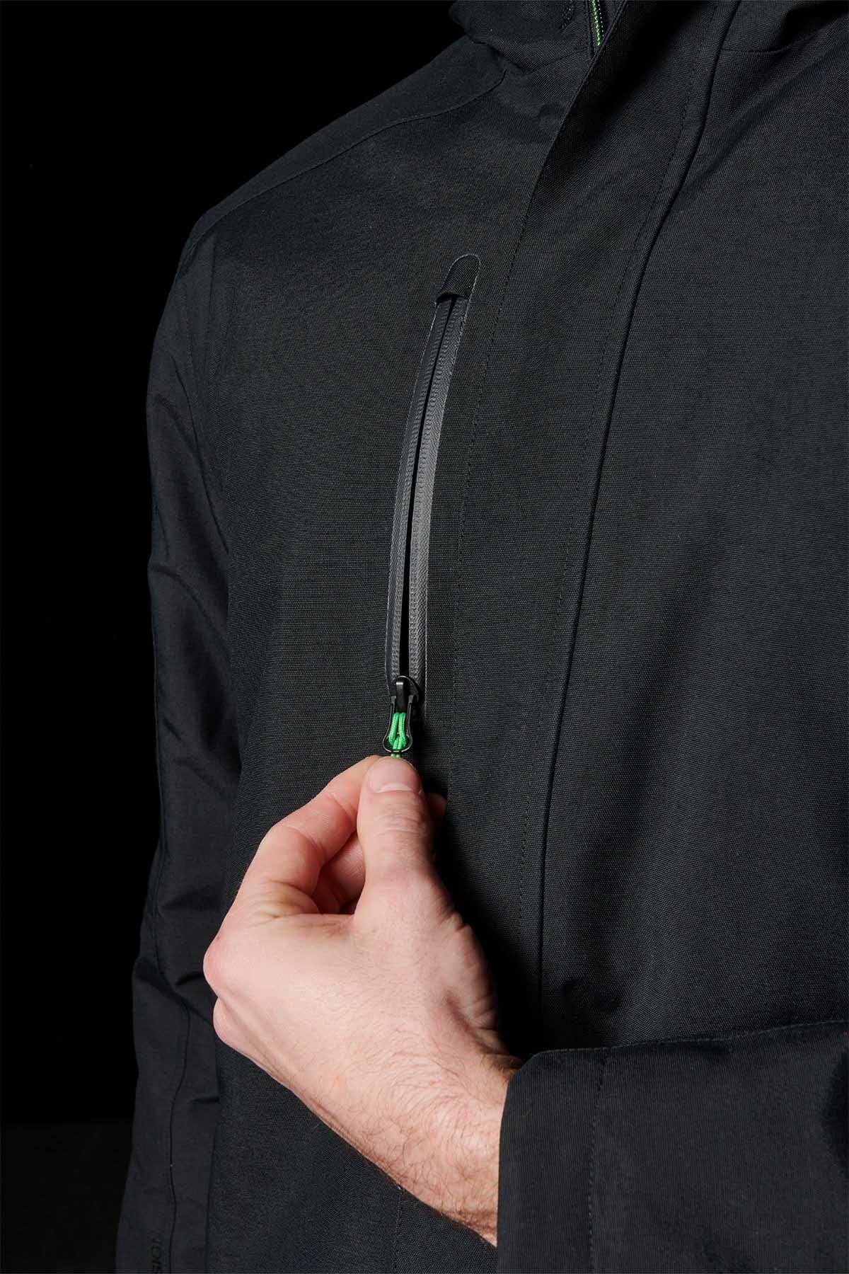 A person’s hand is pulling the zipper on a vertical chest pocket of a black FXD WO-1 Insulated Work Jacket, against a dark background.