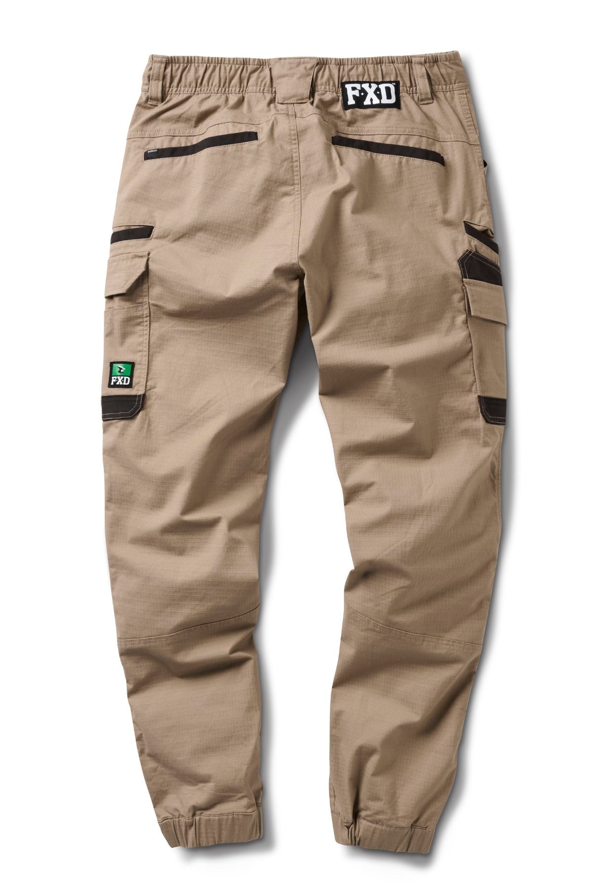 FXD WP-12C tan cargo pants in durable 2-way stretch ripstop with black zipper utility pockets, elastic cuffs, a black FXD waistband logo, and a green FXD patch on the left cargo pocket. Shown laid flat from the back.