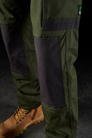 Close-up image of a person wearing FXD WP-1 green work pants with Duratech reinforced pockets, reinforced knee patches, and tan-colored work boots.