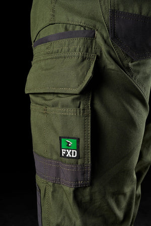 Close-up of dark green FXD WP-1 work pants, showcasing multiple Duratech reinforced pockets and 360-degree stretch for ultimate flexibility. A black tab with a green, red, and white logo and the text "FXD" is visible on one of the pockets. The background is black.