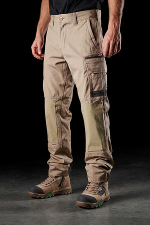 A person wearing the FXD WP-1 beige cargo pants with Duratech reinforced pockets and light brown work boots stands against a black background. Their upper body is not visible in the frame. The comfortable work pant, featuring reinforced knee patches, is slightly wrinkled.