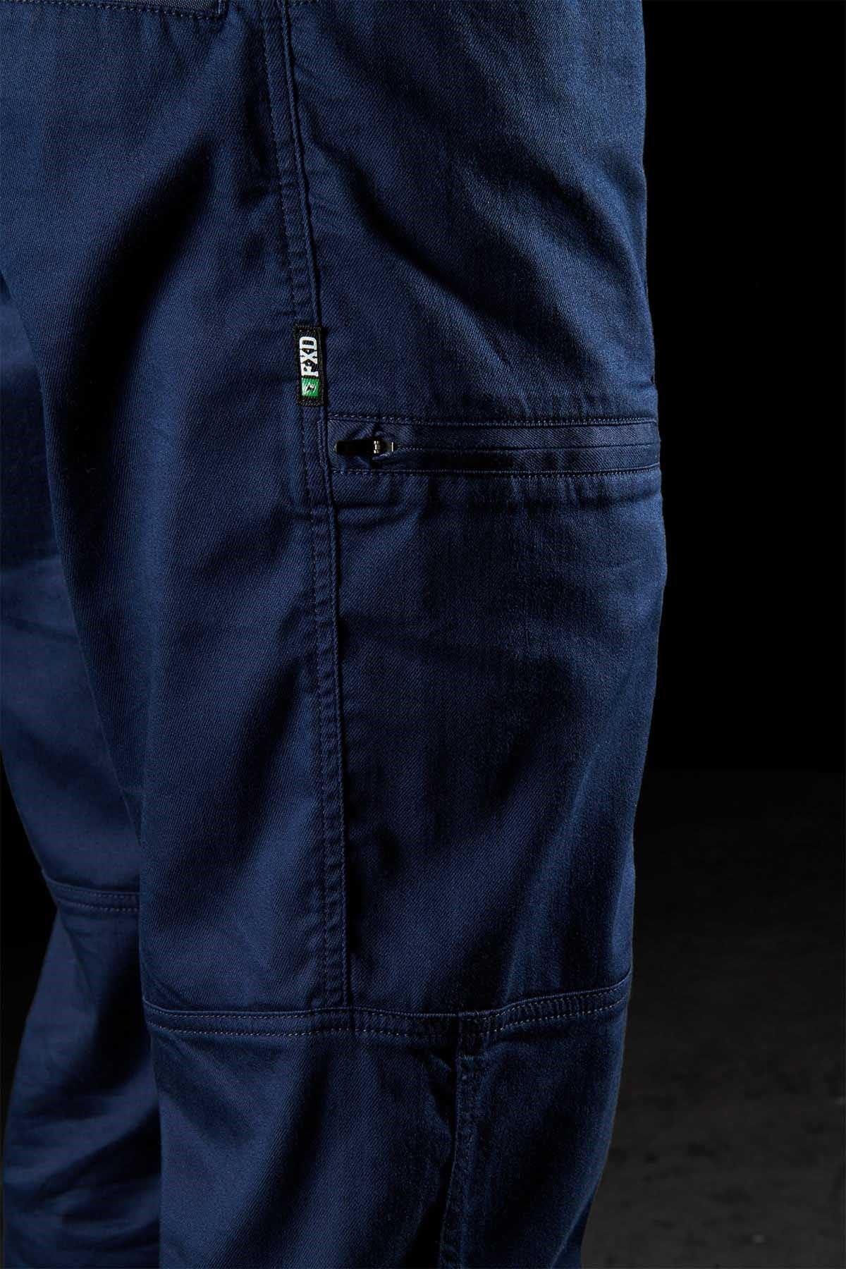 Close-up of the FXD WP-6 navy blue cargo pants, made from stretch nylon twill for durability. Features visible stitching and a small side zipper pocket with a black and green FXD tag. The textured fabric stands out against the dark background.